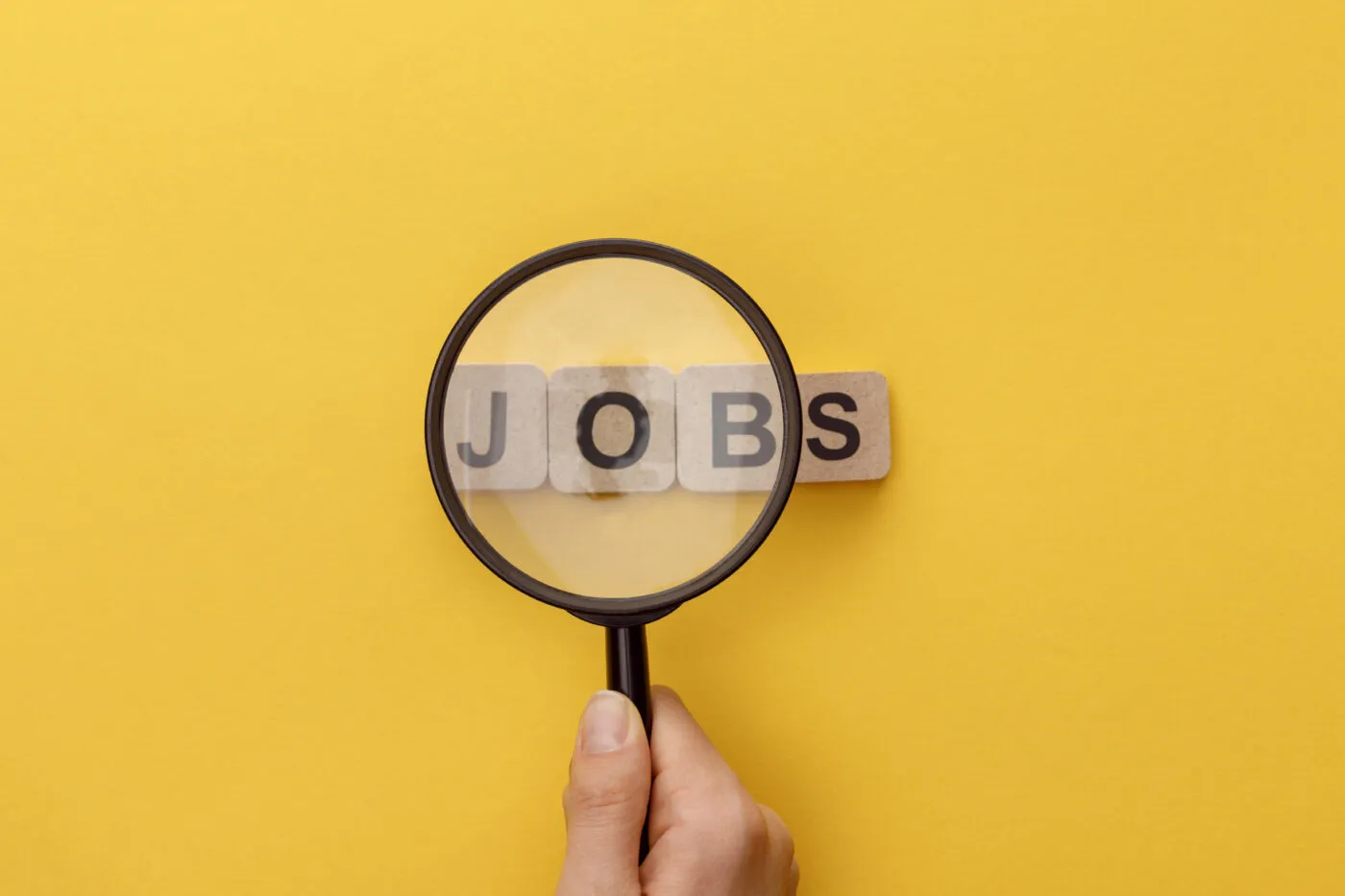 Cropped View Of Woman Holding Magnifying Glass Under Cardboard Squares With Jobs Lettering On Yellow Background