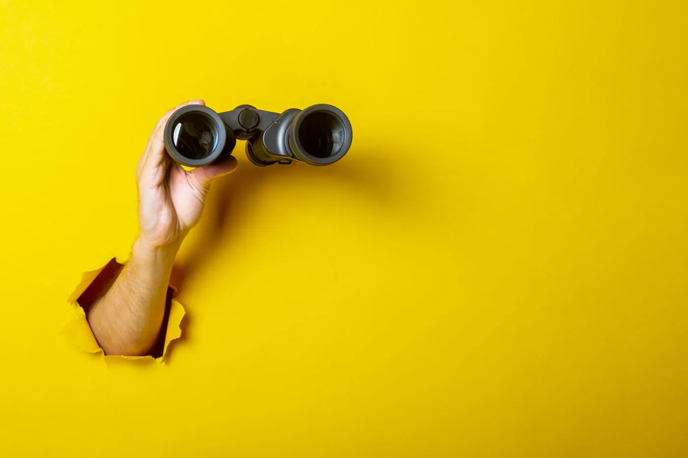 Female Hand Holds Black Binoculars On A Yellow Background. Looki